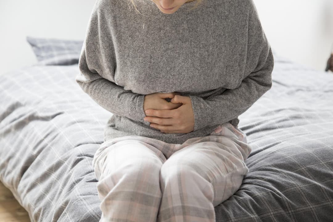 Ilustrație medicală: persoană ținând cu ambele mâini zona abdomenului, sugerând durere sau disconfort digestiv persistent — vizual pentru articolul despre cauzele durerilor de burtă, localizarea simptomelor și când este necesar consultul gastroenterologic.
